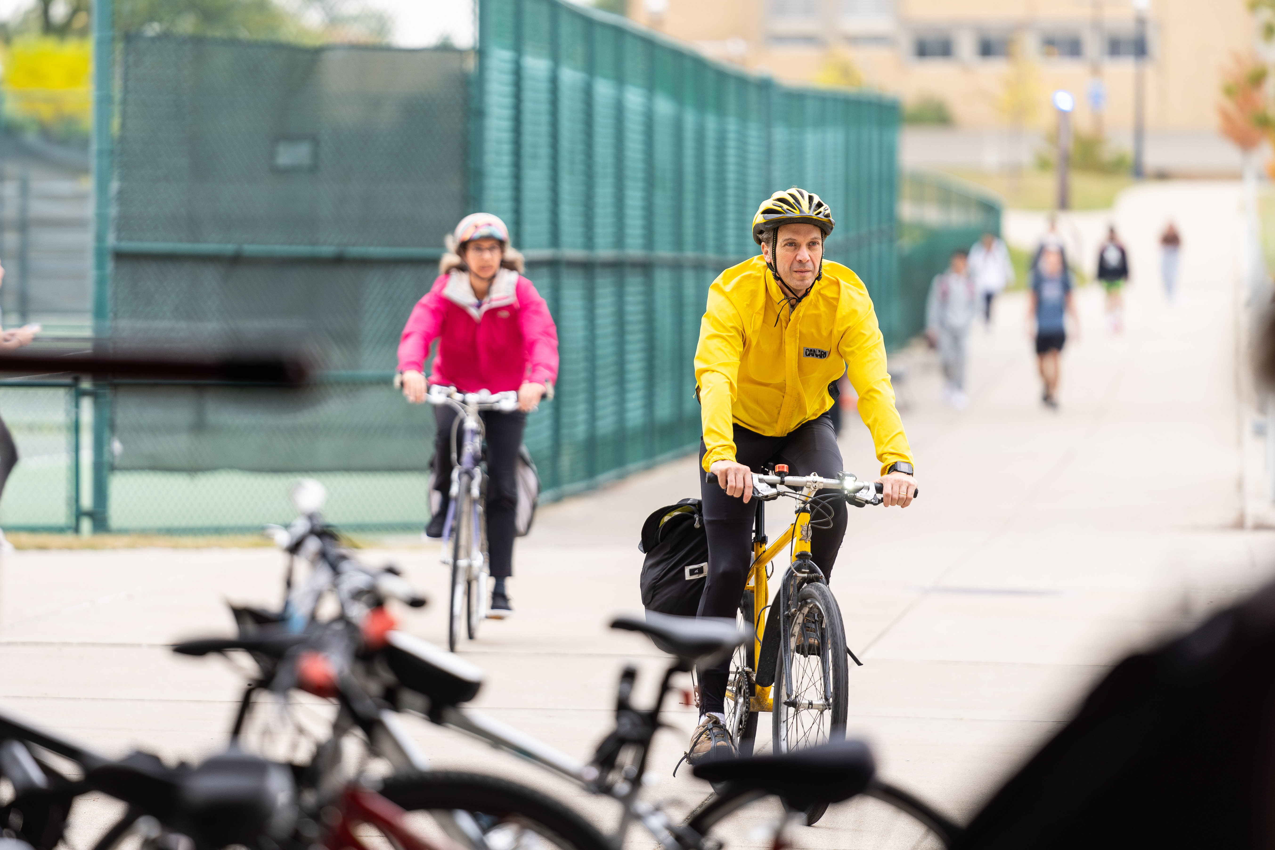 A man in a bright yellow jacket and woman in pink jacket are seen riding bicycles.
