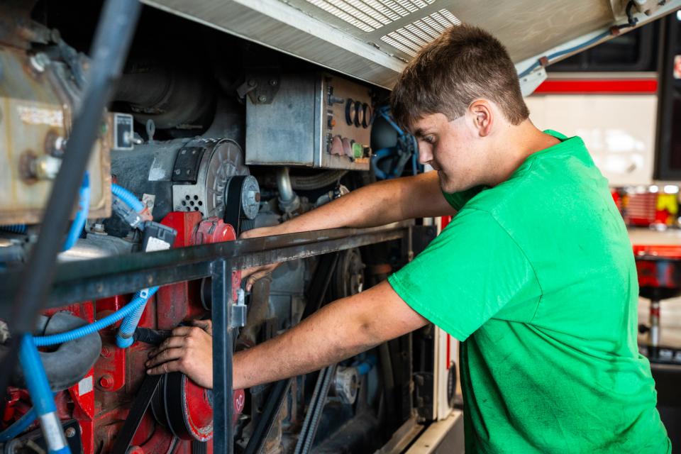 A student wearing a green shirt works on a bus under the hood.